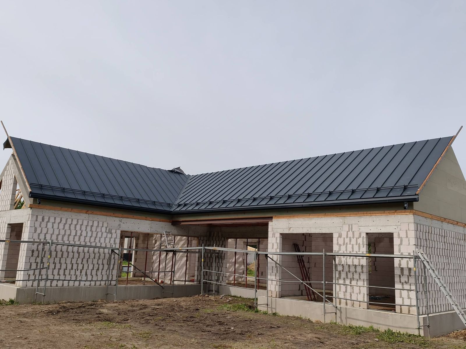 Užbaigtas L formos namo stogas su tamsia valcuota skarda